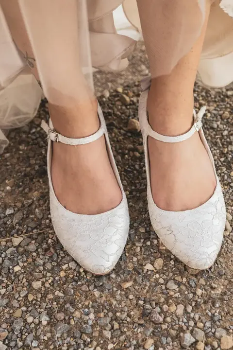 Brautschuhe mit Glitzer auf Kies, darüber der Saum des Brautkleids