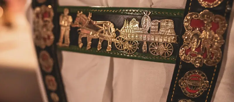 Nahaufnahme eines bestickten Sennen-Hosenträgers mit Alpaufzug-Motiv in Messing, Detail einer Hochzeit in Tracht