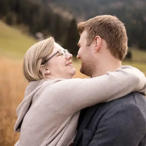 Paar umarmt sich lachend im herbstlichen Gras, Paarshooting am Schwendisee im Toggenburg